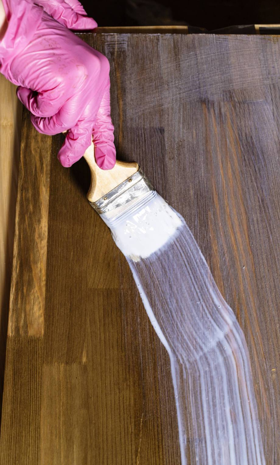 gloved hand varnishes a stained pine furniture board at home